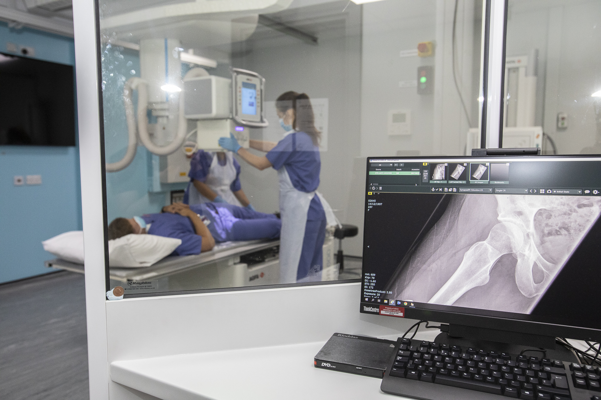 Screen displaying X-ray scan with clinicians in the background operating x-ray equipment