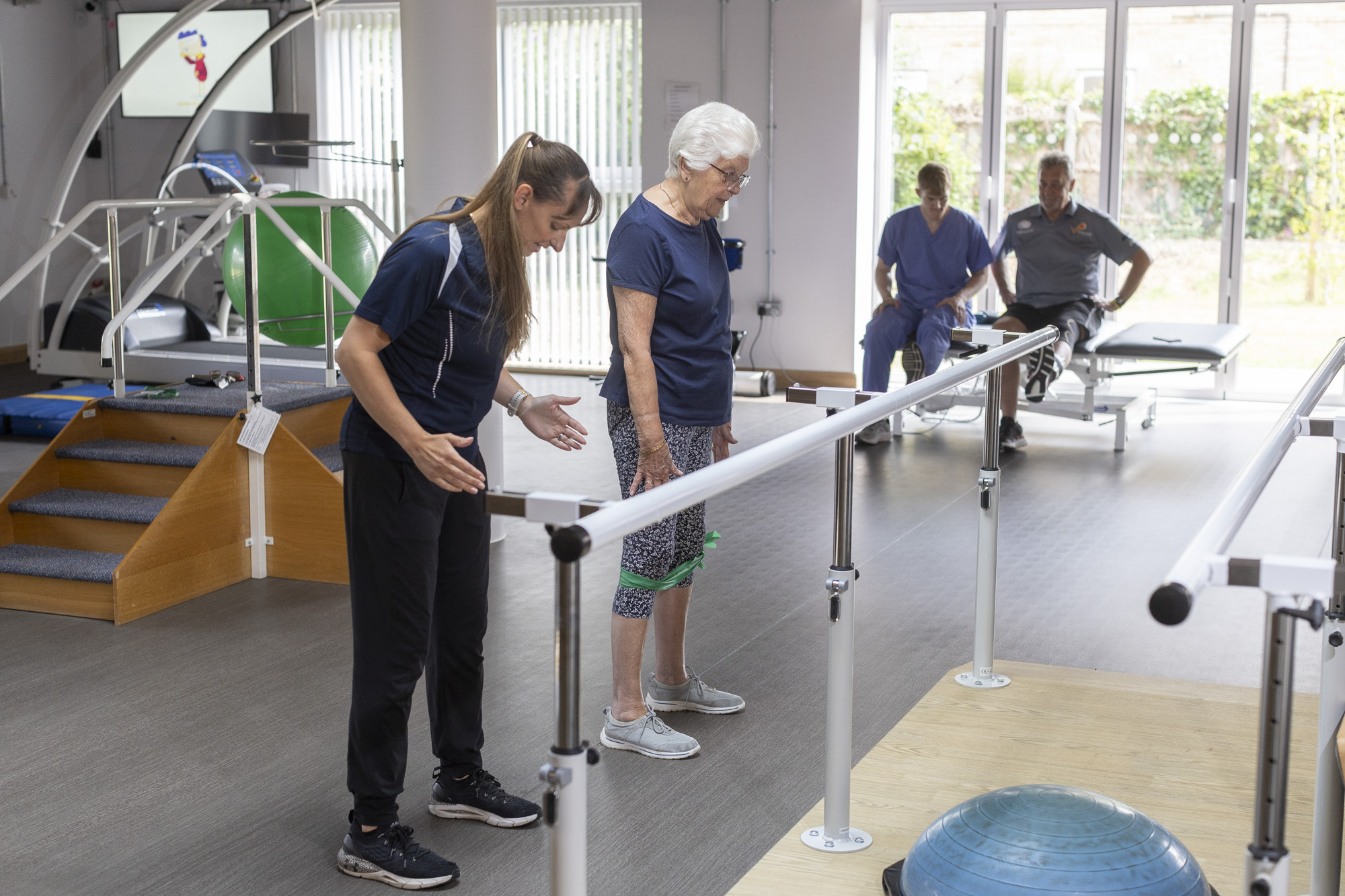 Consultant and Patient going through an exercise routine with a theraband. A man in the background is going through a similar exercise with a student chiropractor