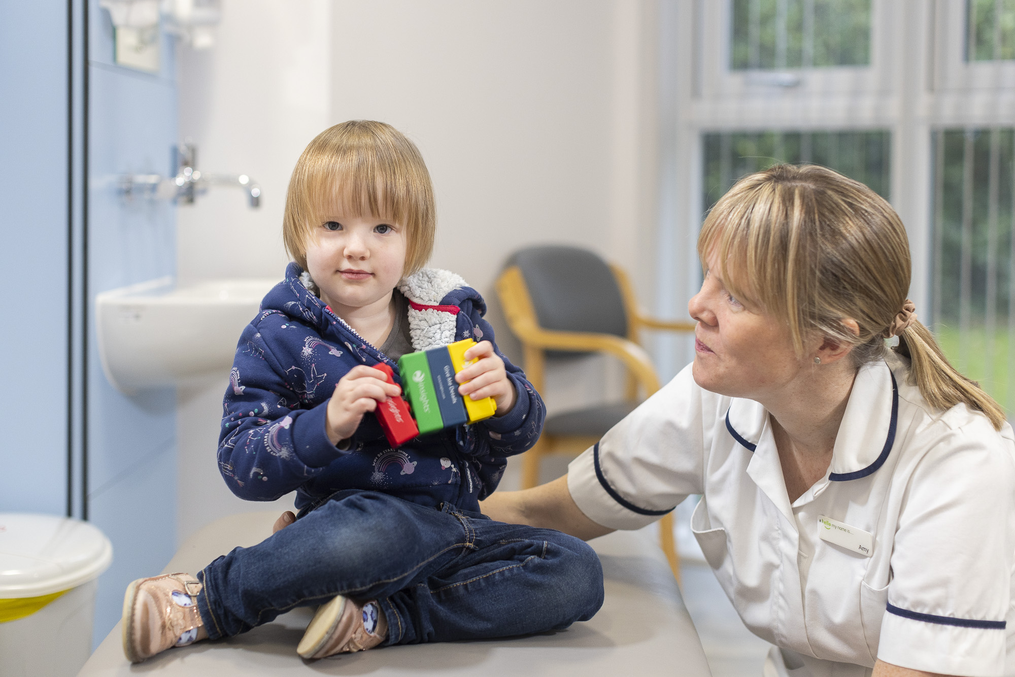 Child in paediatric clinic holding coloured blocks looking directly at camera