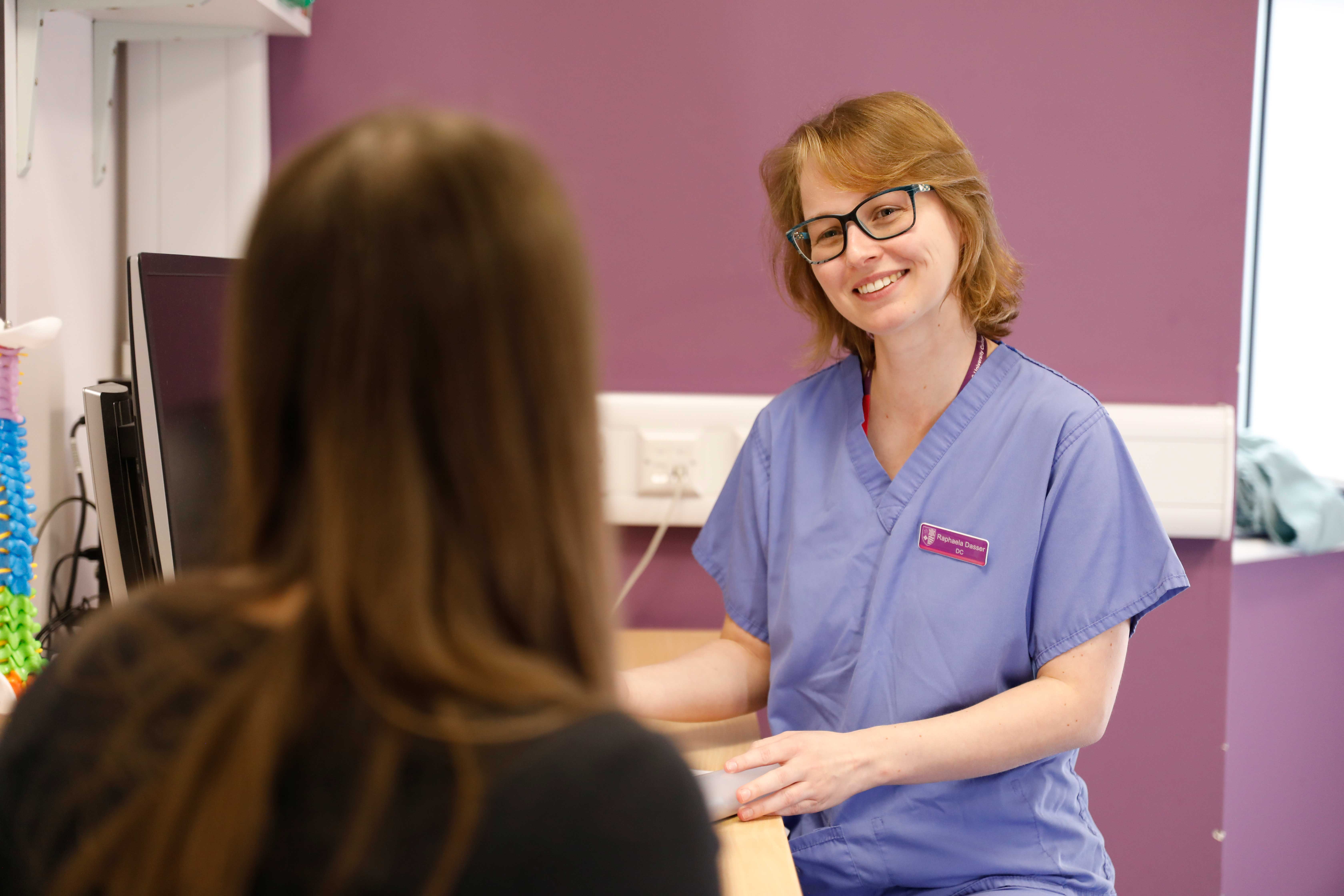 Over the shoulder image of female chiropractor with her head titled to one side, she listens to female patient