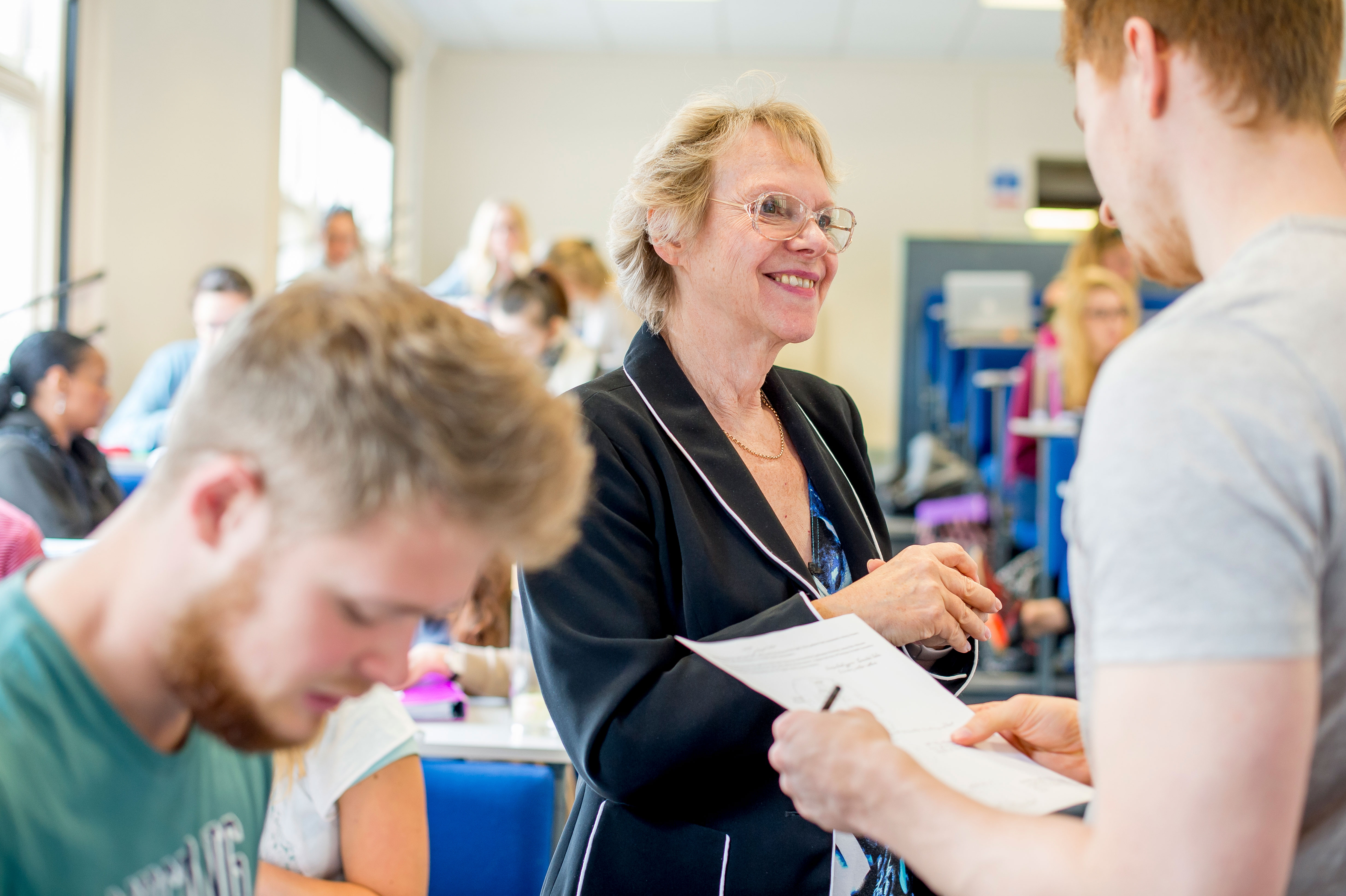 A woman shakes the hand of a young health professional in training, they are in a university environment