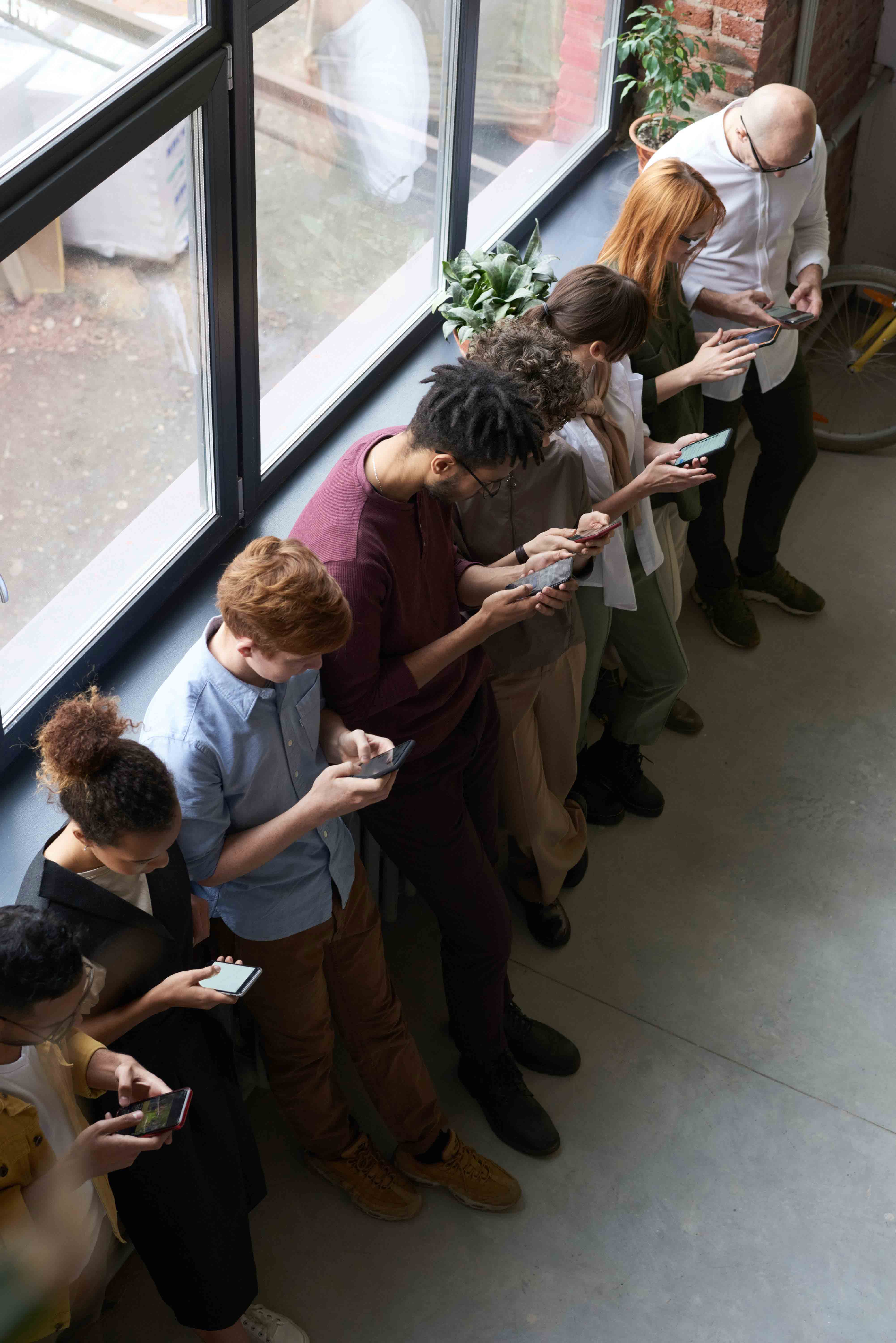 People standing in a line all craning their necks to look at their phones